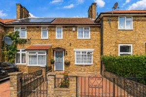 Brick terraced house with blue door, small front garden, and ornate iron gate; brick driveway and neighboring homes under a blue sky.