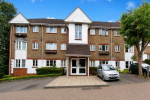 Three-story brick apartment building with white trim and central entrance, parked cars, and blue sky above.