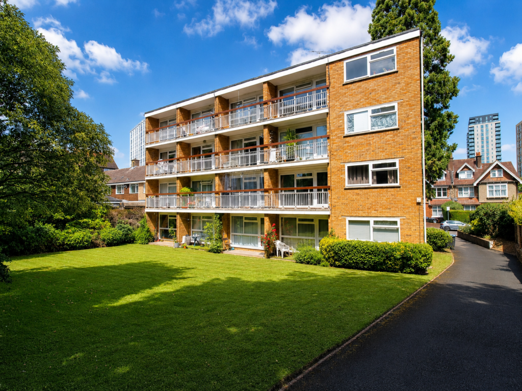 Brick apartment building with balconies and a green lawn, blue sky and a paved path nearby.