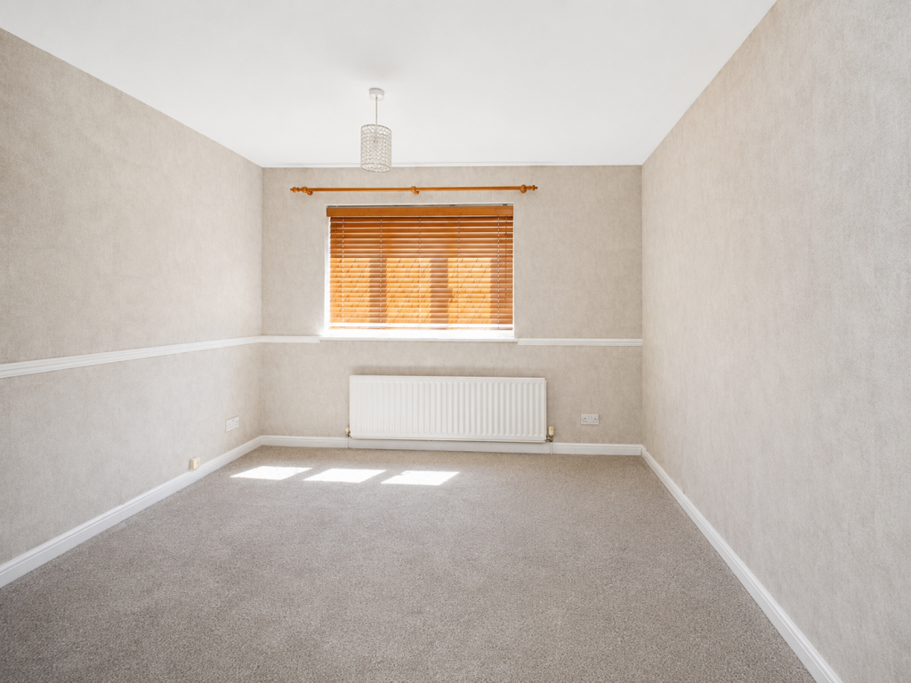 Empty beige-walled room with a window covered by wooden blinds, a radiator beneath, and a pendant light overhead.