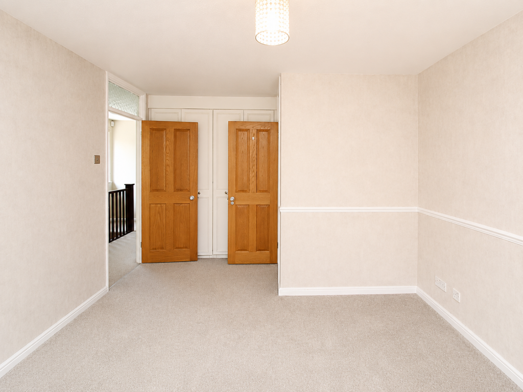 A beige empty room with carpet, two wooden doors open at the back, and white built-in closets beyond them, seen from the foreground.
