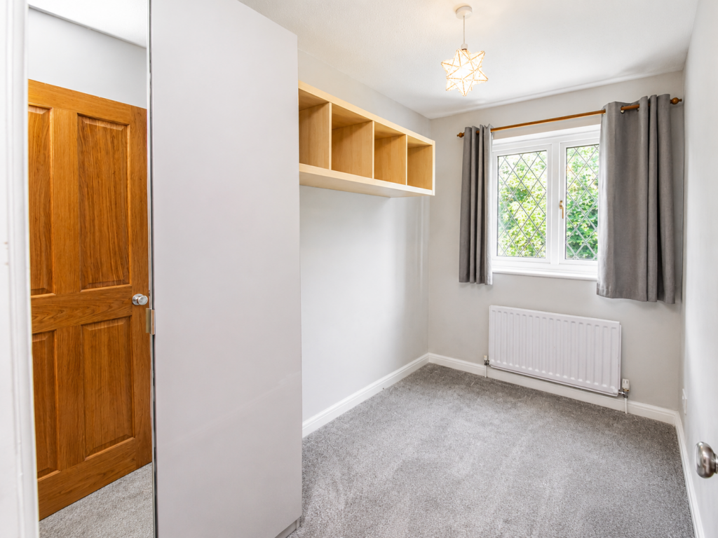 Small bedroom with a tall white wardrobe, four open cubby shelves, and a wooden door on the left; neutral gray walls.