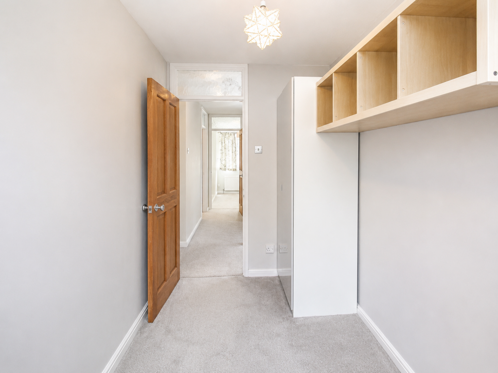 Narrow hallway with beige carpet, an open wooden door on the left, and light wood cubby shelves on the right under a pendant light.