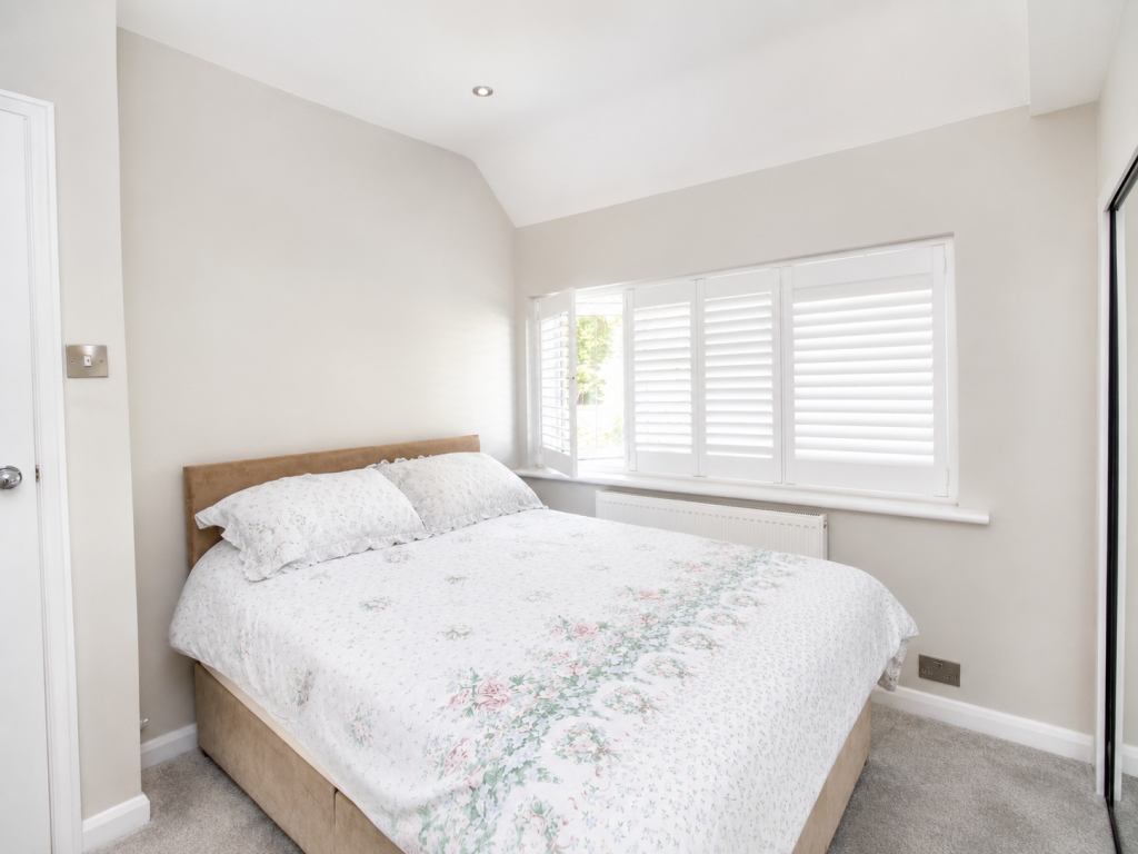 Bedroom with a queen bed, beige headboard, floral quilt, and white shuttered windows along the wall