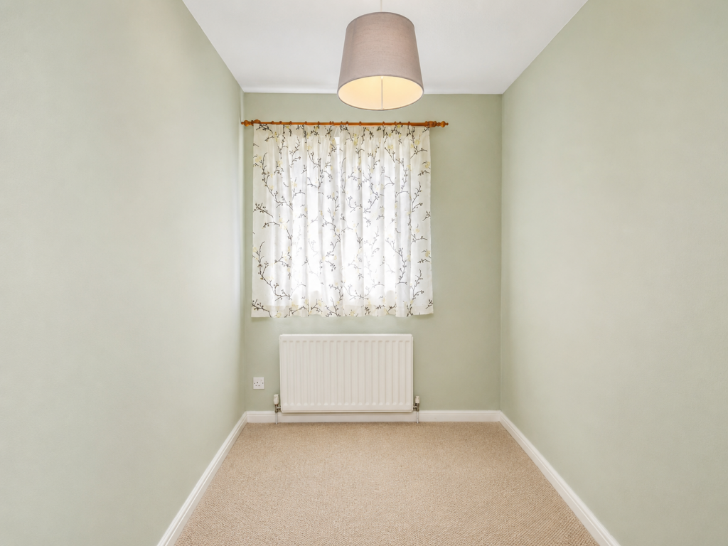 Small, narrow, softly lit room with pale green walls, a window with floral curtains, and a white radiator below.