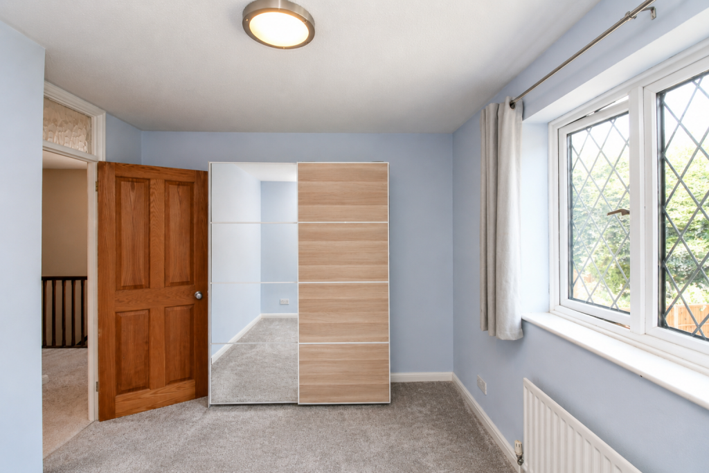 Blue bedroom with a two-tone sliding wardrobe, open wooden door to a hallway, and a window with a radiator below it.
