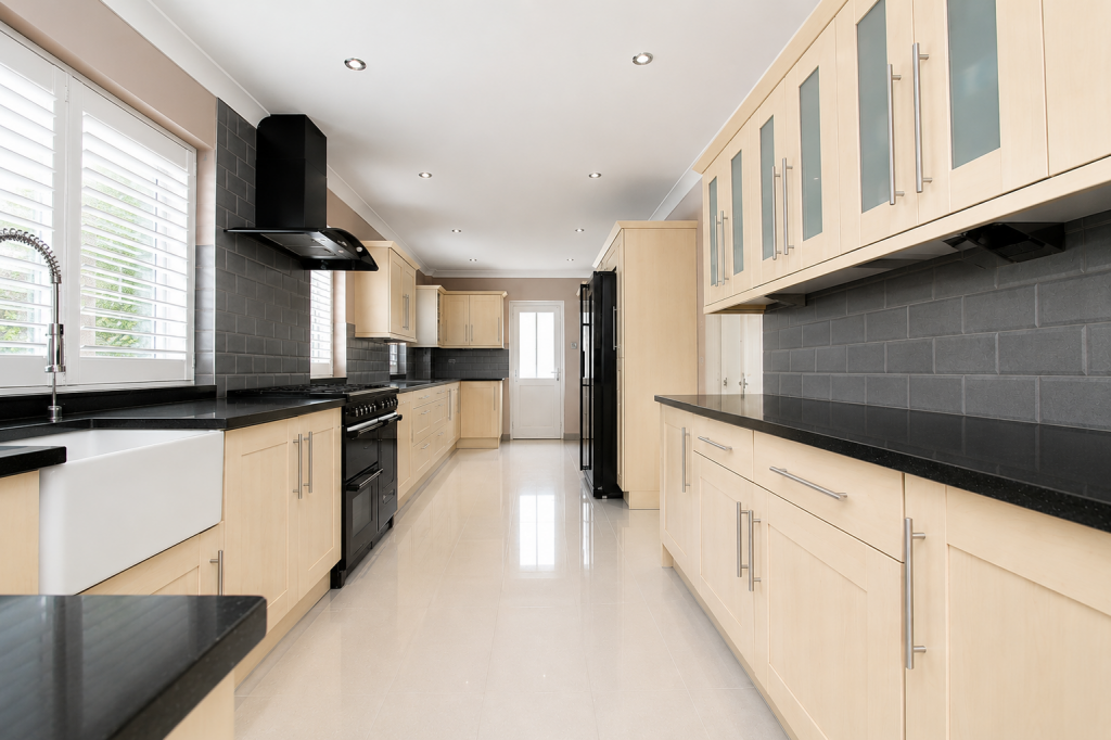 Modern kitchen with light wood cabinets, black countertops, and gray tile backsplash along a long galley layout.