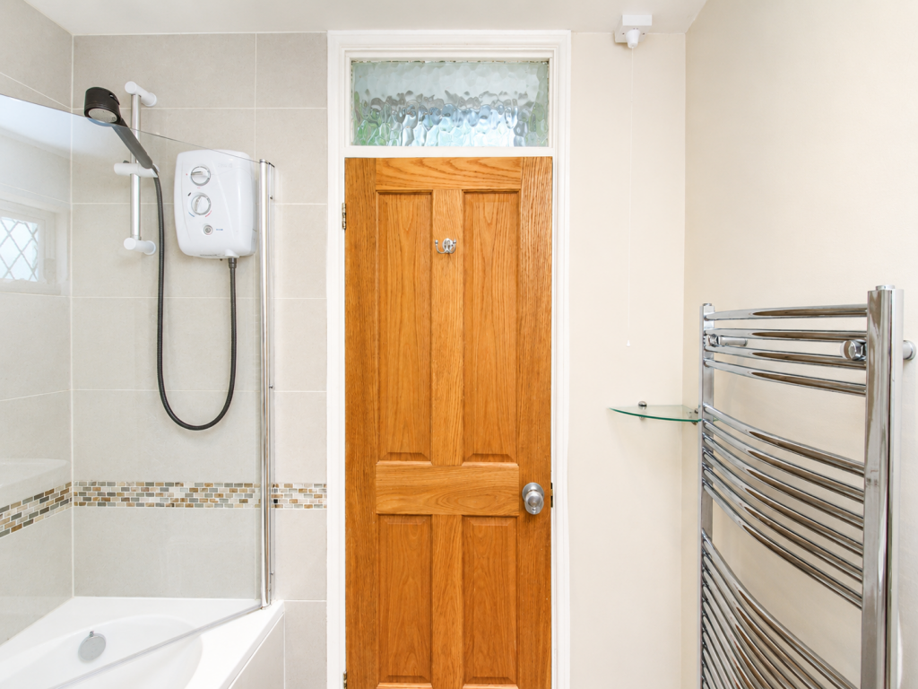 Wooden bathroom door with frosted transom window above, flanked by a tiled shower area and chrome towel heater to the right