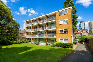 Brick apartment building with four stories and balconies, set in a green lawn under a bright blue sky.