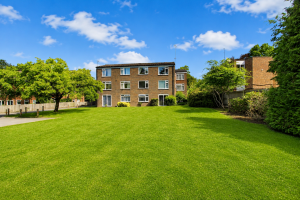 Three-story brick apartment building facing a wide green lawn under a bright blue sky with scattered clouds.