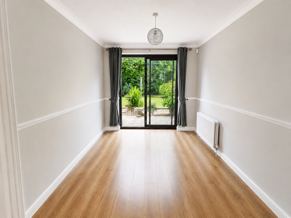 Empty rectangular living room with light gray walls, wooden floor, and a sliding glass door to a green garden outside; dark gray curtains pulled to sides.