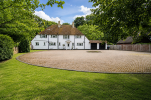 White country house with a brown tiled roof, circular gravel driveway, and green lawn with trees framing the scene.