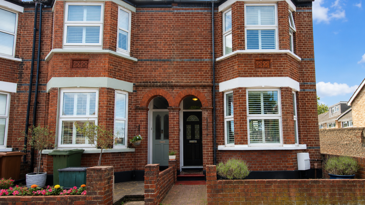 Two brick townhouse entrances under arched doorway, with bay windows on either side and a small front garden with potted plants.