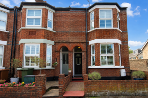 Two brick townhouse entrances under arched doorway, with bay windows on either side and a small front garden with potted plants.