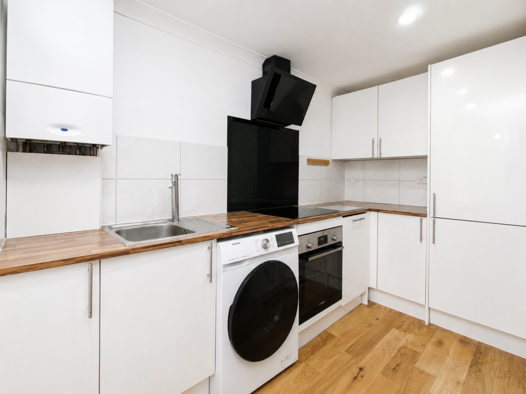 Contemporary white kitchen with wood countertops, built-in oven and washing machine, and a black chimney-style range hood.