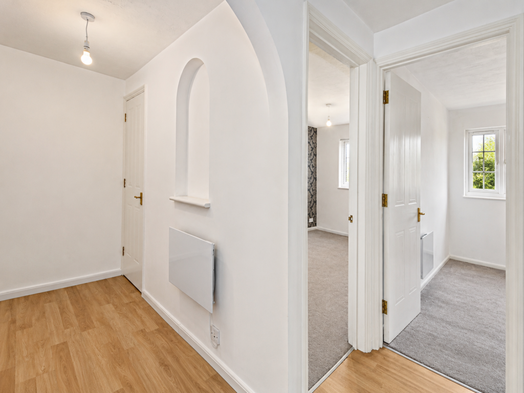 White hallway with a curved wall niche, radiator, and light bulb fixture; doorways lead to carpeted rooms with a window visible outside.