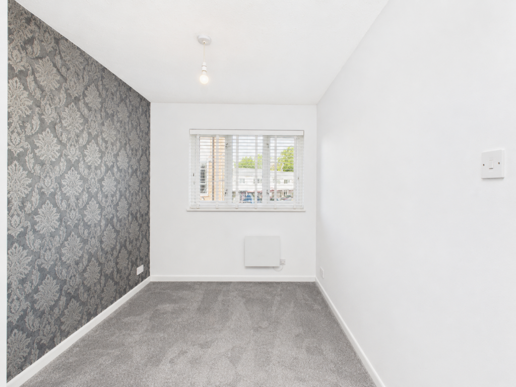 Small empty room with a gray patterned accent wall on the left, white walls, a window with blinds, and gray carpet.